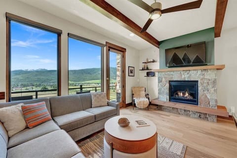 Relax in a bright, stylish living area with vaulted ceilings, warm wood beams, a cozy fireplace, and expansive windows framing beautiful Eden mountain views.