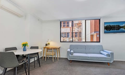 Open-plan living area with a sofa bed, dining table, and window allowing natural light.