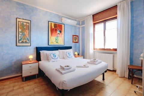 A double room with a lively and welcoming design, with walls decorated in shades of sky blue and functional furnishings for a relaxing stay. The double bed is large and comfortable, complete with quality linens and comfortable pillows. The natural light coming in through the window creates a pleasant and peaceful atmosphere, ideal for resting after a day spent visiting the attractions of Lake Garda.