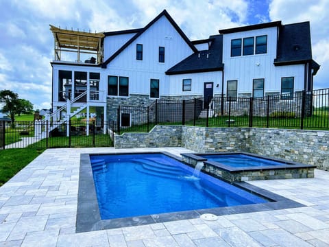 Pool and Spa - Resort-style pool and raised spa with natural stone surround, bluestone paver patio, and the modern farmhouse beyond.