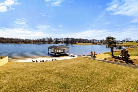 Expansive Backyard: Beautifully manicured lawn gently slopes down to a private sandy beach, dock, and play area, all framed by stunning panoramic views of Lake Anna.