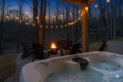 Private hot tub at Austen — tucked under the covered lower deck, string lights overhead, wooded setting, striped towels provided