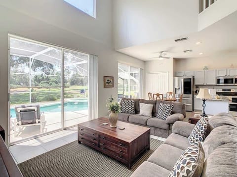 Spacious living area with plush seating, high ceilings, and large windows overlooking the private pool and screened-in lanai, with easy access to the kitchen and dining areas.