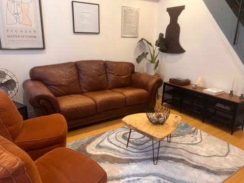Cozy living space with a leather sofa, warm chairs, and artistic, homey touches.