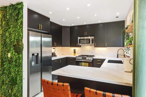 Enjoy a chef’s dream kitchen with sleek black cabinets, marble countertops, and high-end appliances. A lush green accent wall adds a fresh touch, while the open layout makes cooking a breeze. Perfect for food lovers and entertainers. 