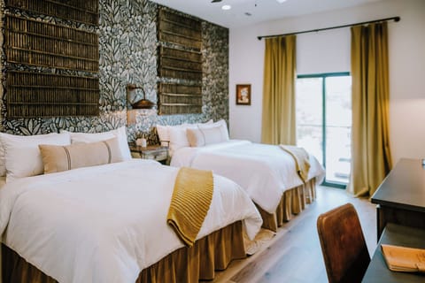Inside the Lazy Spur Suite — two queen beds, natural light through curated drapery, and modern Western design upstairs at Gaines Ranch on the Square.