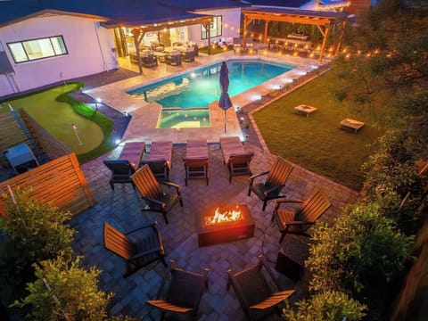 Aerial view of the property at night featuring an illuminated swimming pool, hot tub, outdoor fire pit, multiple lounge areas, and landscaped grounds ideal for evening relaxation.
