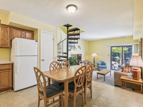 This charming Bethany Beach townhome features a family-friendly layout with a cozy living space adorned with natural light, a spiral staircase, and direct access to a private terrace overlooking lush greenery.