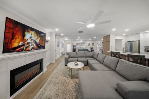 The living room has an electric fireplace, flat screen TV, and multiple seats.