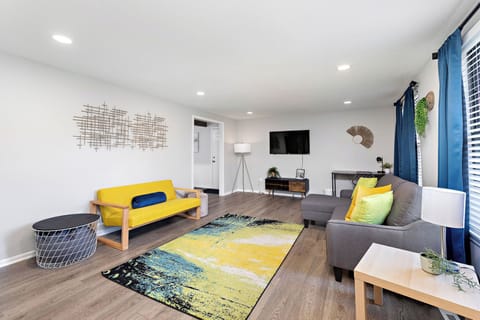 A bright and airy living room featuring a vibrant yellow sofa, a comfortable gray sectional, and a colorful abstract rug.