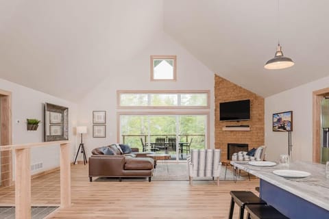 Open concept living room, kitchen, and dining room with modern decor. Features a gas fireplace below a smart tv. 