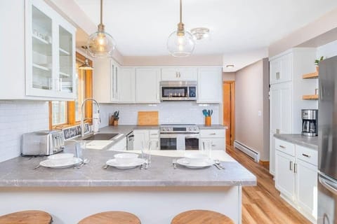 A modern kitchen with stainless steel appliances, fully stocked with cookware, dishes, and utensils. A spacious island with bar stools offers a perfect spot for dining or gathering while cooking.