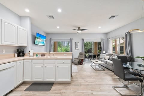 Bright open-concept kitchen and living area with white cabinetry, updated flooring, comfortable seating, and sliding glass doors bringing in natural light.