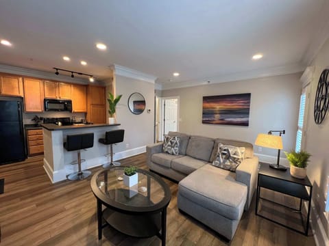 Inviting living room featuring a cozy sectional, sleek coffee table, and soft lighting. An open layout connects seamlessly to the kitchen, creating a welcoming space for any stay.