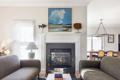 Cozy living area with a modern fireplace, artwork above the mantel, and soft seating. The space is filled with natural light and leads into the dining area, creating a warm and inviting atmosphere.







