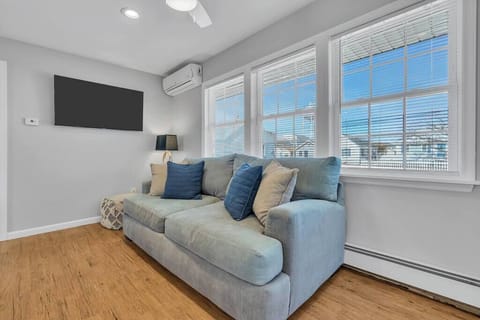 Family room with sectional, blue throw pillows, mounted TV, AC unit, and triple windows.