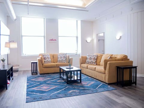 - Bright living room with comfy sofas and tall windows inviting natural light 
- Stylish rug and spacious layout perfect for relaxing and gathering 
- Modern downtown apartment offering an inviting stay for guests 
