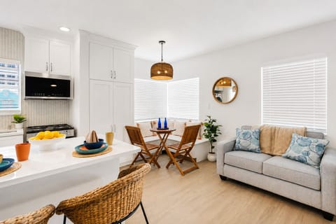 Bright, open-concept living area with plush seating, smart TV, and a cozy dining nook for four. Coastal decor and warm wood tones create a relaxed, beachy feel — the perfect spot to unwind after a day at the beach.