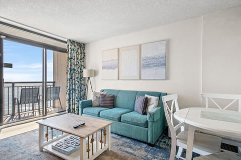 Oceanfront living room with a cozy full-size sofa, coastal décor, and dining space, opening to a private balcony. Wake to Atlantic sunrises, panoramic ocean views, and soothing waves in this bright beachfront retreat.