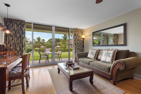 Relax on the comfortable sofa while gazing through floor-to-ceiling glass doors at lush tropical gardens and your private patio with outdoor seating—perfect for morning coffee or evening unwind.