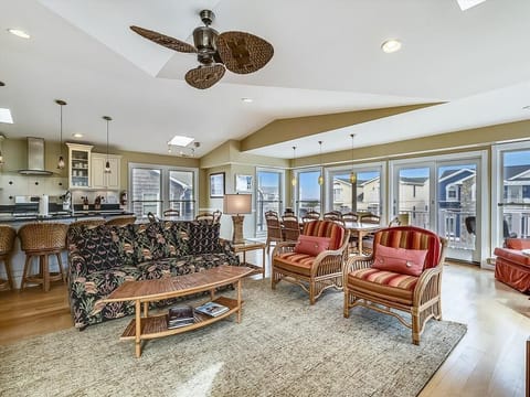 The open living area showcases a vibrant tropical print sofa and cozy wicker chairs, complemented by expansive windows offering scenic views.