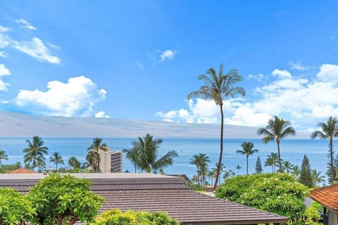 Stunning ocean-view lanai framed by lush tropical greenery and swaying palm trees, offering panoramic vistas of the sparkling blue waters and clear skies.