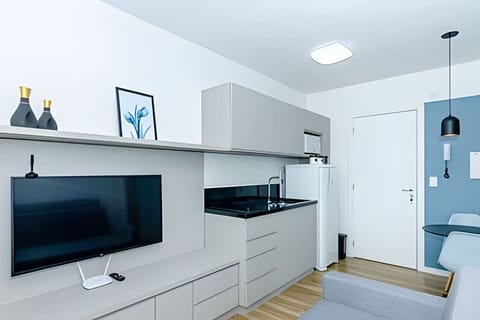 Sala/Cozinha com televisão, cooktop de indução, pia, geladeira e armários.