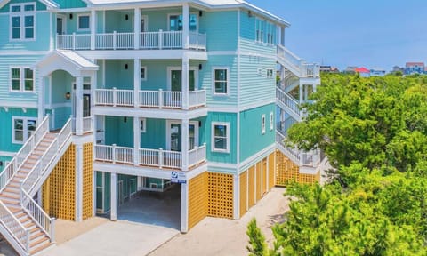 This striking three-story coastal vacation home features bright turquoise siding, multiple spacious balconies, and elevated design nestled amid lush greenery.