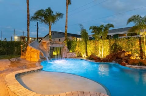 Twilight view of the resort-style pool with tanning shelf, waterfall and grotto