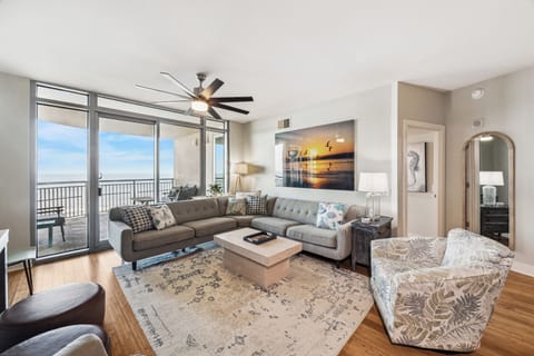 Bright and spacious living area with stunning Gulf views, featuring a large sectional, coastal decor, and access to a private balcony.