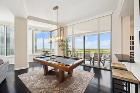 Entertainment space includes a custom pool table set under modern lighting, surrounded by panoramic windows showcasing sweeping bay penthouse views and direct access to three private balconies.
