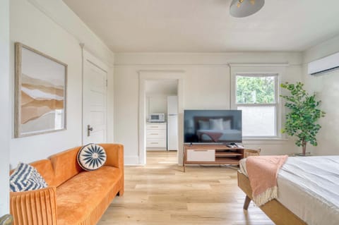 Living area with orange loveseat, TV, and bed nearby.