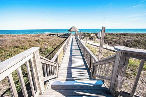 A serene wooden boardwalk leading to the beach, with a gazebo at the end and a peaceful coastal landscape in the background.