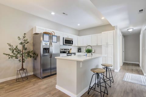 The modern kitchen features stainless steel appliances, bright white cabinetry, and a central island with bar seating—perfect for morning coffee or evening prep.