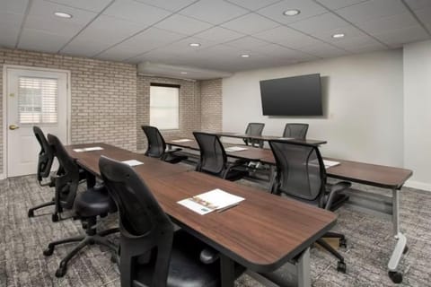 Meeting room with boardroom-style dark wood tables, black office chairs, an exposed brick wall, and a wall-mounted TV