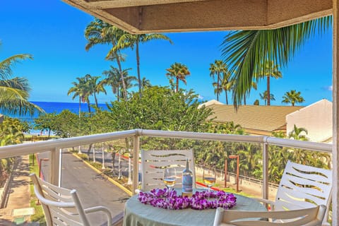 Open and airy balcony overlooks the coast with ocean view framed by palm trees.