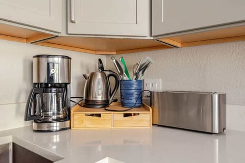 Coffee maker, kettle, toaster, utensils on white countertop with sleek cabinets and modern kitchen setup.