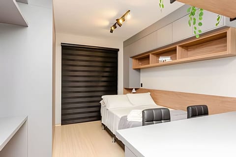 Quarto com cama de casal, blackout na janela para noite de sono revigorantes e balcão com duas cadeiras.