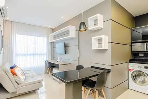 Sala de estar com balcão 2 cadeiras para alimentação, um sofá confortável, mesa de leitura/reunião e televisão smart.