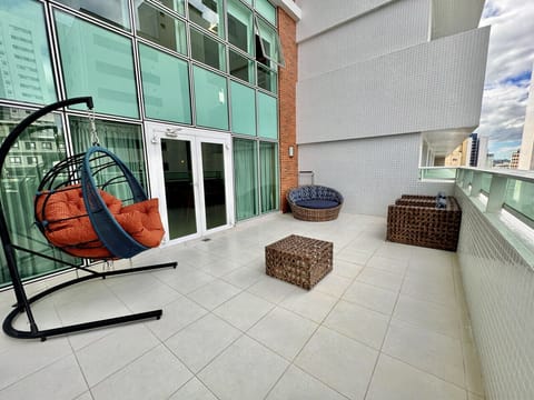 Varanda com cadeira suspensa de balanço, apoio de pé e poltronas.