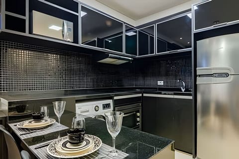 Cozinha equipada com utensílios de café da tarde, micro-ondas, lava e seca, forno, cooktop, exaustor, geladeira e pia.