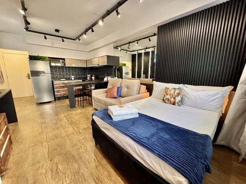 Studio iluminado com cama de casal e cozinha integrada ao fundo