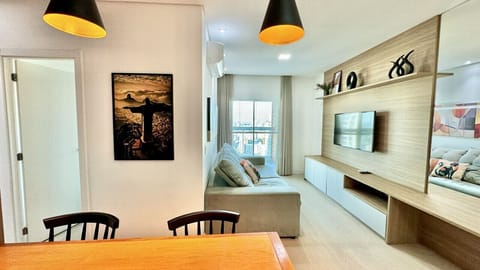 Sala de estar com sofa, mesa de jantar e TV na parede