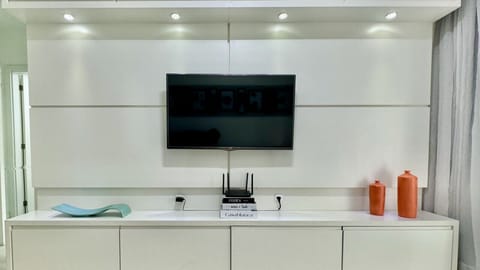 Sala com TV preta na parede e bancada branca com decoracao minimalista