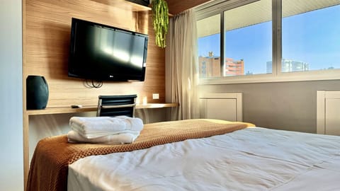 Quarto espaçoso com cama de casal, TV na parede e grande janela com vista