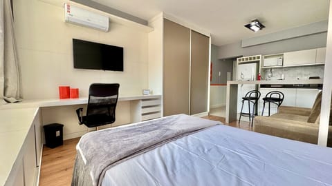 Quarto com cama de casal, TV na parede e kitchenette integrada