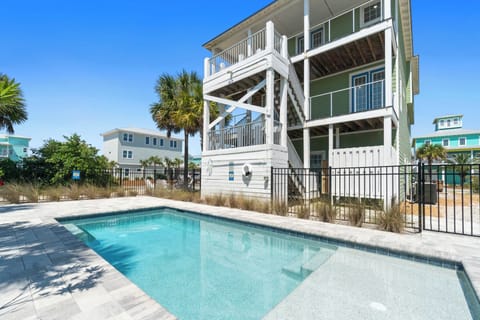 Coastal beach house featuring private swimming pool with tropical palm trees and multi-level balconies in sunny vacation community.