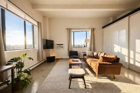 Welcome to your sun-drenched corner studio, featuring a plush queen bed and wall-to-wall windows.