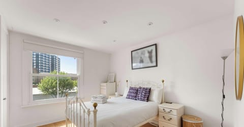 This bright and airy primary bedroom offers a serene and restful atmosphere. The room features a classic white metal bed frame dressed in crisp white linens, perfectly complemented by a pair of elegant three-drawer bedside tables.