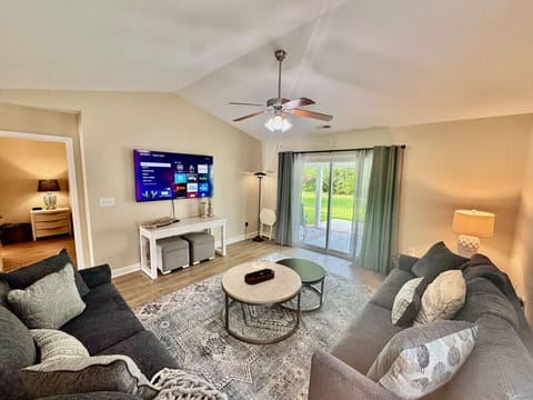 Spacious Living room with large smart TV, ceiling fan, new furniture, and access to covered back patio.